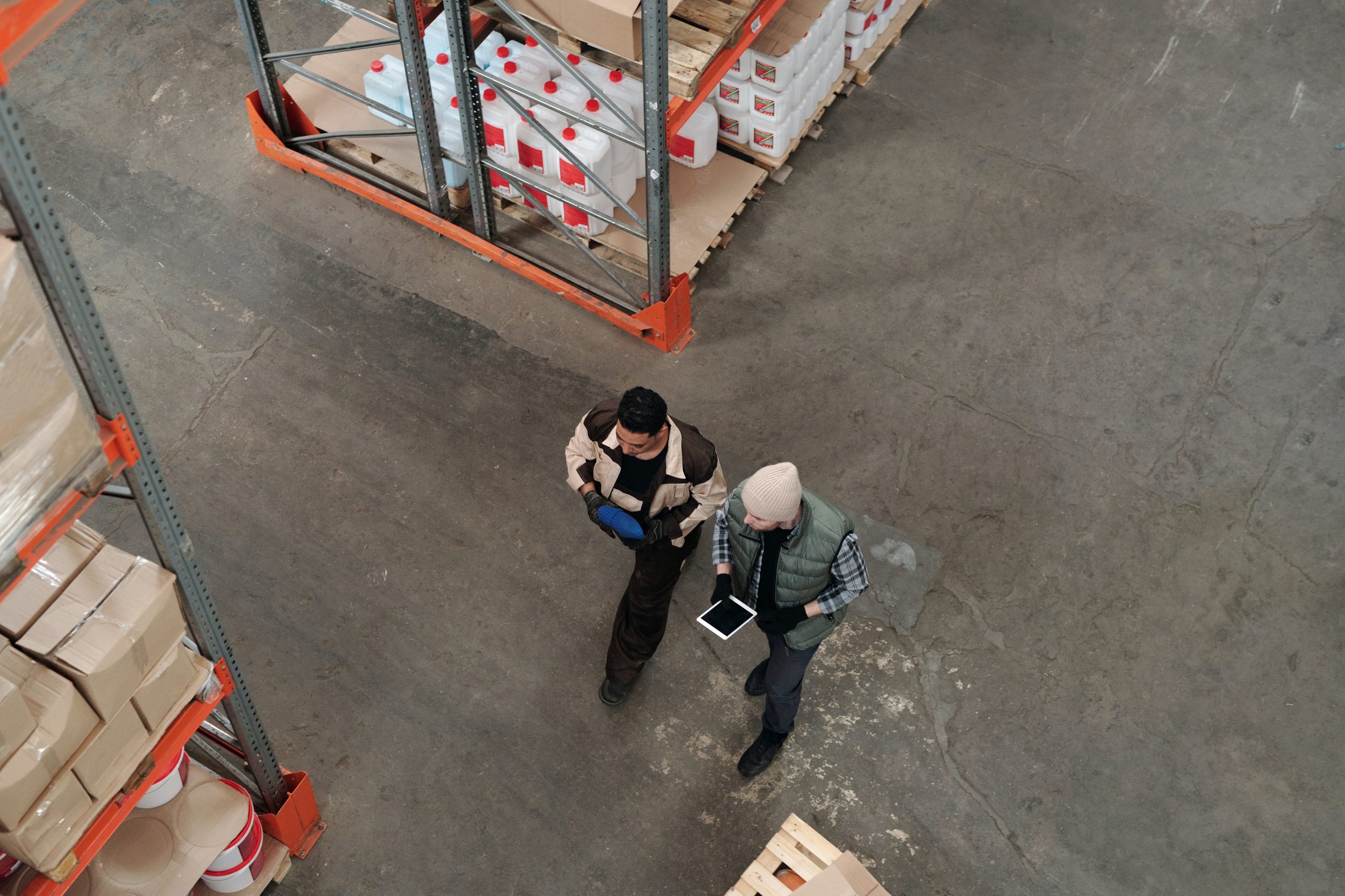 Two men walking through a distribution warehouse working on mobile tablets